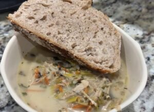 Wild rice chicken soup with vegetables served in a white bowl with sourdough bread