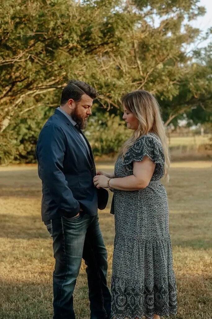 Married Christian couple standing together outdoors, holding hands in a field at sunset.